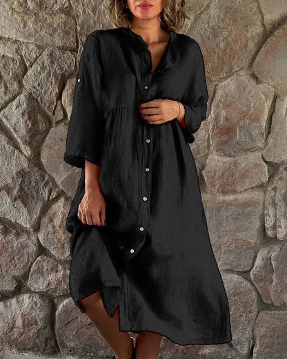 Black - A woman wearing a vibrant fuchsia pink linen midi dress with a button-down front, roll-tab sleeves, and an empire waist, standing against a stone wall.