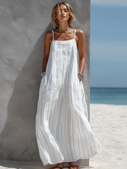White - Woman standing on a beach wearing a relaxed fit, striped spaghetti-strap maxi dress with her hands in the side pockets.