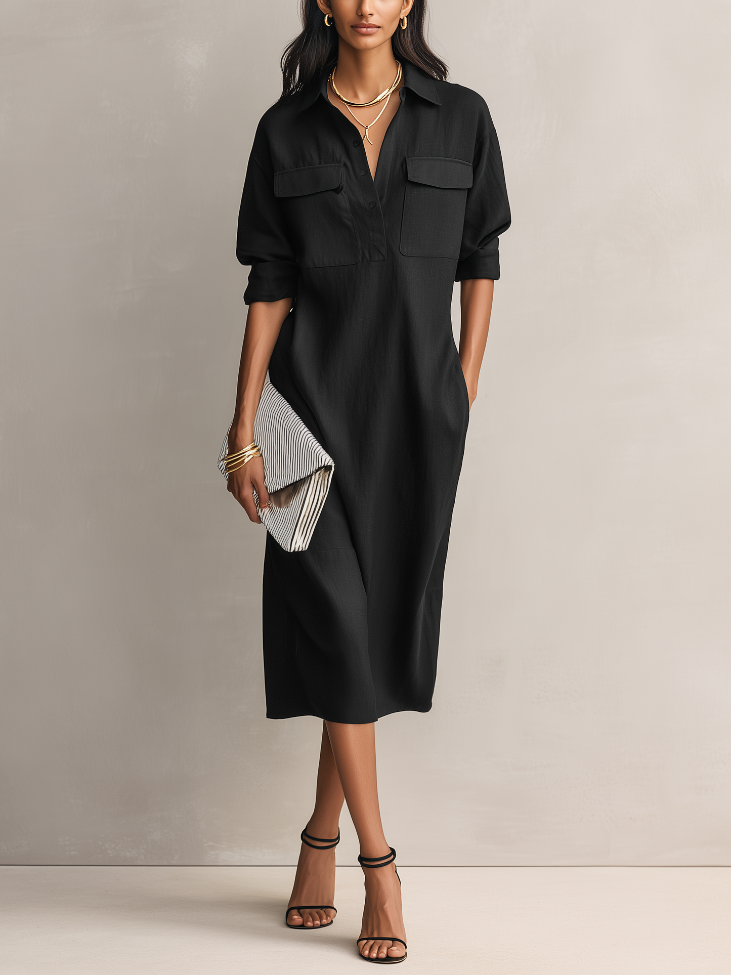 Black - Model wearing a relaxed fit collared midi shirtdress with chest pockets and rolled sleeves, styled with gold jewelry and strappy heels