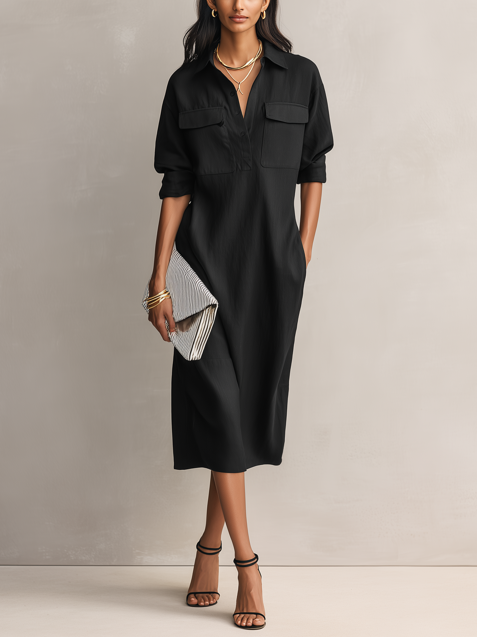 Black - Model wearing a relaxed fit collared midi shirtdress with chest pockets and rolled sleeves, styled with gold jewelry and strappy heels