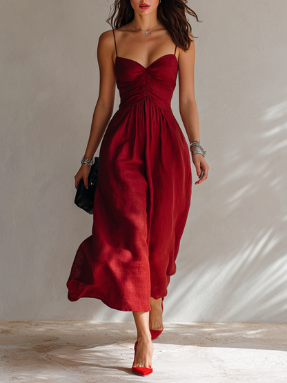 Red - A woman walking in a textured midi dress featuring a ruched bodice, sweetheart neckline, and delicate spaghetti straps.