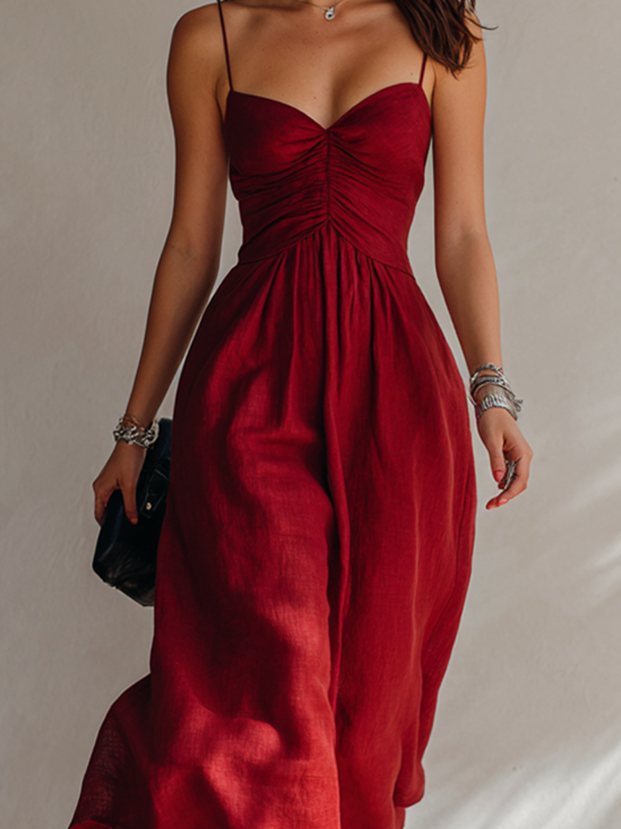 Red - A woman walking in a textured midi dress featuring a ruched bodice, sweetheart neckline, and delicate spaghetti straps.
