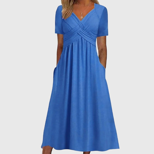 Blue - A woman wearing a cornflower blue midi-length jersey dress featuring a criss-cross ruched bodice, short sleeves, and a flowy skirt with side pockets.