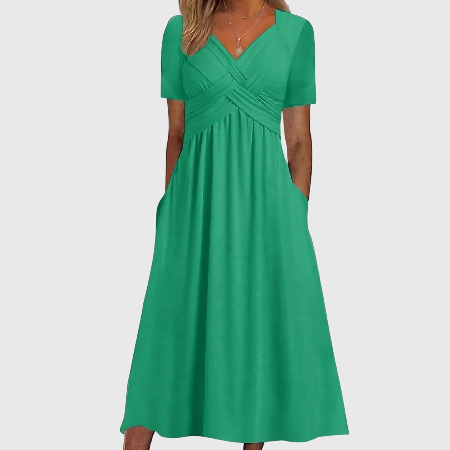 Green - A woman wearing a cornflower blue midi-length jersey dress featuring a criss-cross ruched bodice, short sleeves, and a flowy skirt with side pockets.