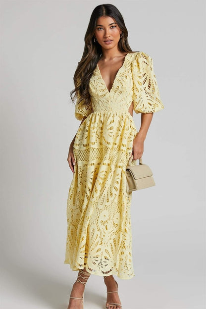 Woman in yellow lace maxi dress with puff sleeves and cut-out waist.