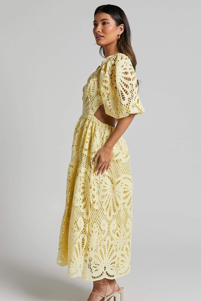 Woman in yellow lace maxi dress with puff sleeves and cut-out waist.