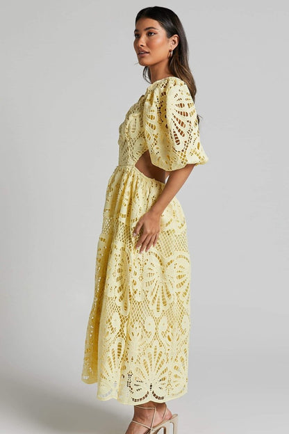 Woman in yellow lace maxi dress with puff sleeves and cut-out waist.