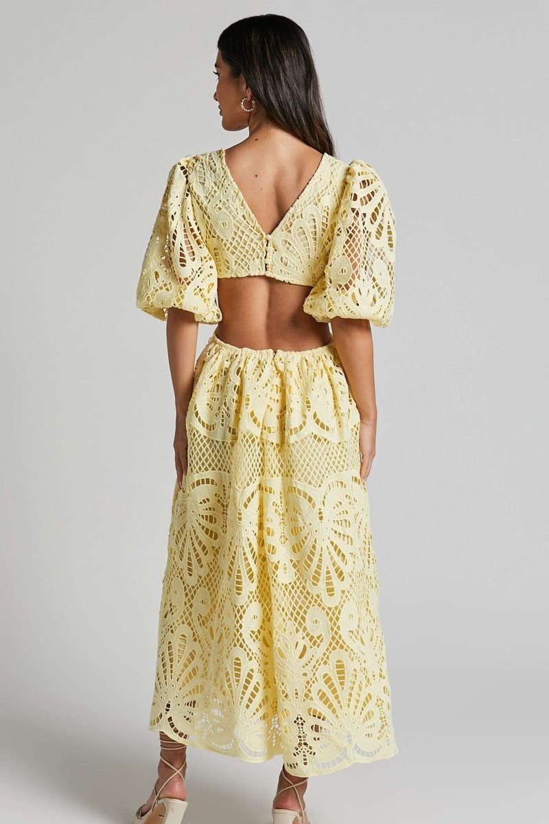 Woman in yellow lace maxi dress with puff sleeves and cut-out waist.