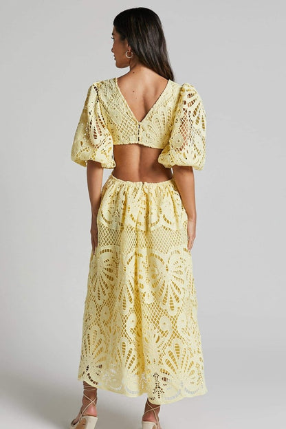 Woman in yellow lace maxi dress with puff sleeves and cut-out waist.