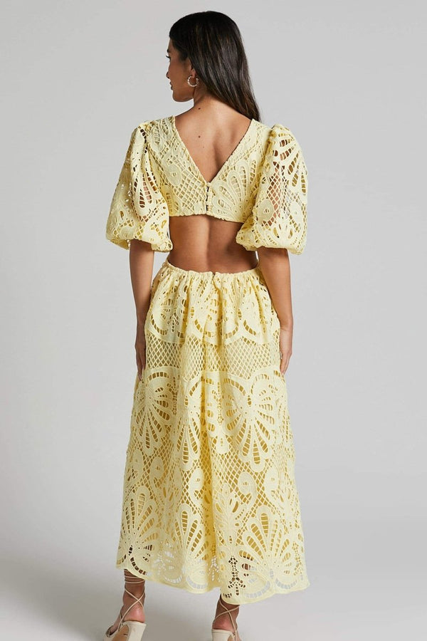 Woman in yellow lace maxi dress with puff sleeves and cut-out waist.