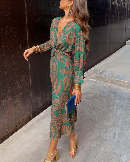 Green - A woman wearing a blue and bronze botanical print satin midi dress with a deep V-neck, twist-front waist, and long sleeves.