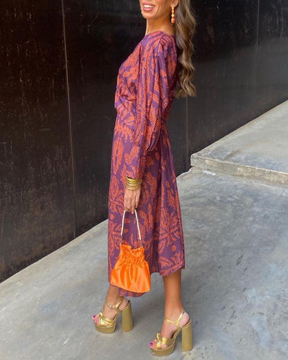 Purple - A woman wearing a blue and bronze botanical print satin midi dress with a deep V-neck, twist-front waist, and long sleeves.