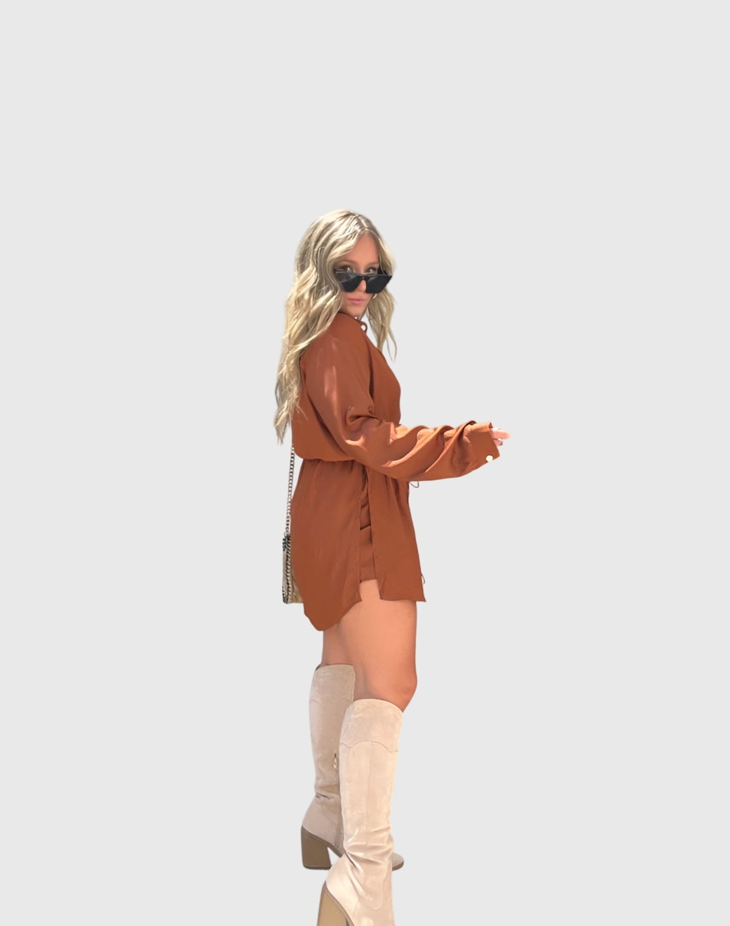 Pink - A woman wearing a long-sleeve burgundy satin romper with a button-down front, pointed collar, and cinched waist, styled with knee-high beige boots.