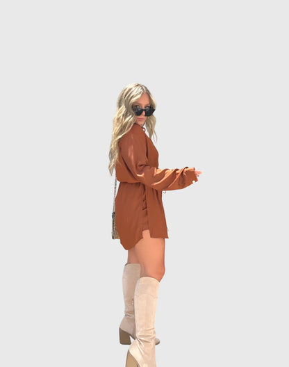 Pink - A woman wearing a long-sleeve burgundy satin romper with a button-down front, pointed collar, and cinched waist, styled with knee-high beige boots.
