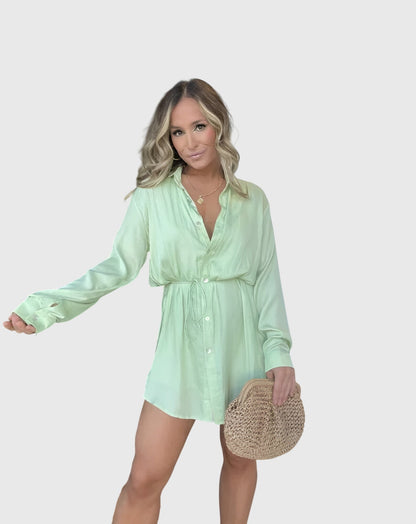 Melon - A woman wearing a long-sleeve burgundy satin romper with a button-down front, pointed collar, and cinched waist, styled with knee-high beige boots.