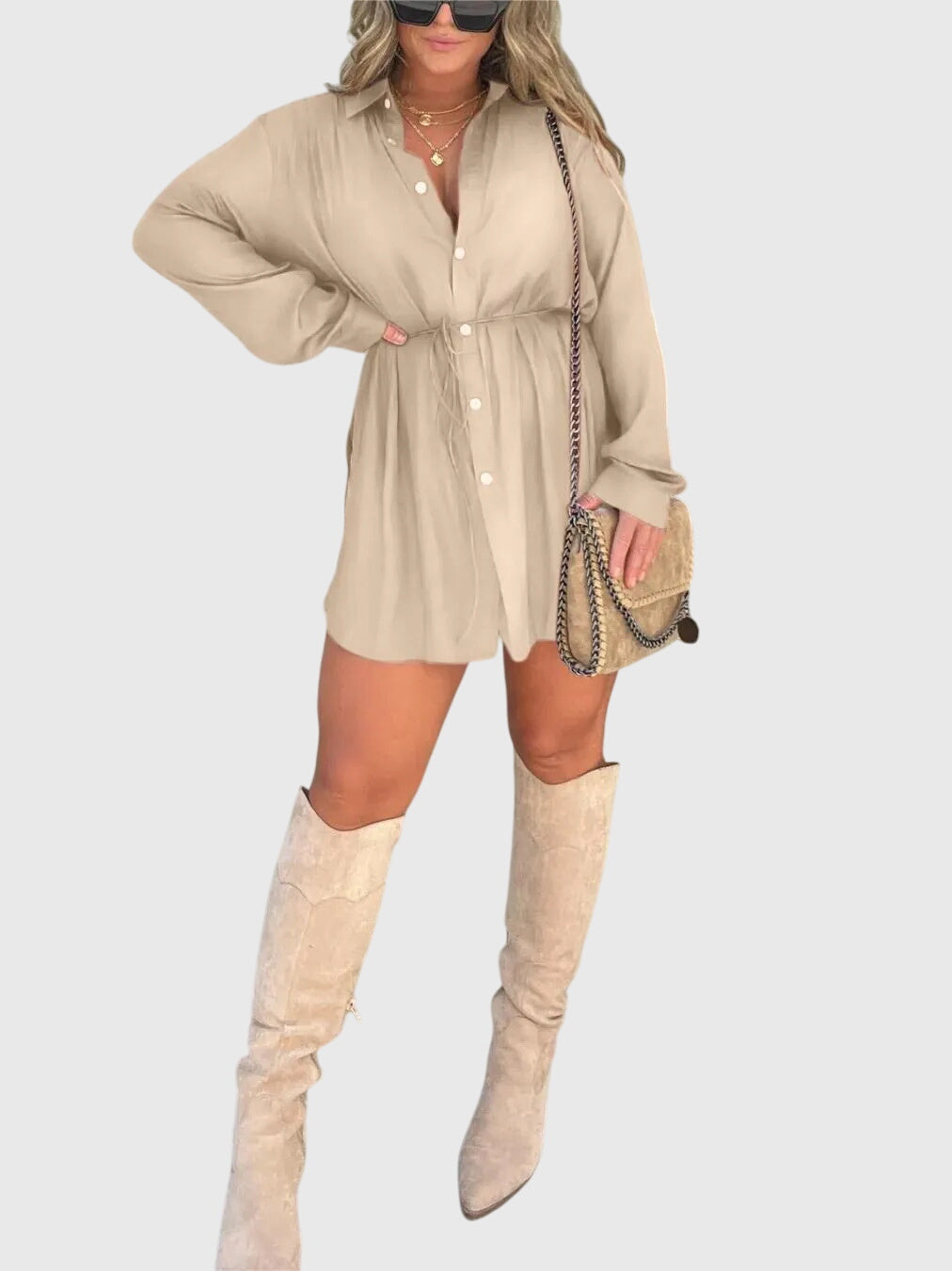Apricot - A woman wearing a long-sleeve burgundy satin romper with a button-down front, pointed collar, and cinched waist, styled with knee-high beige boots.