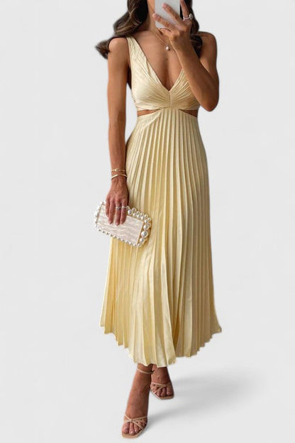 A woman wearing a pale yellow pleated satin midi dress with a plunging V-neckline and side waist cutouts, holding a pearl-embellished clutch.