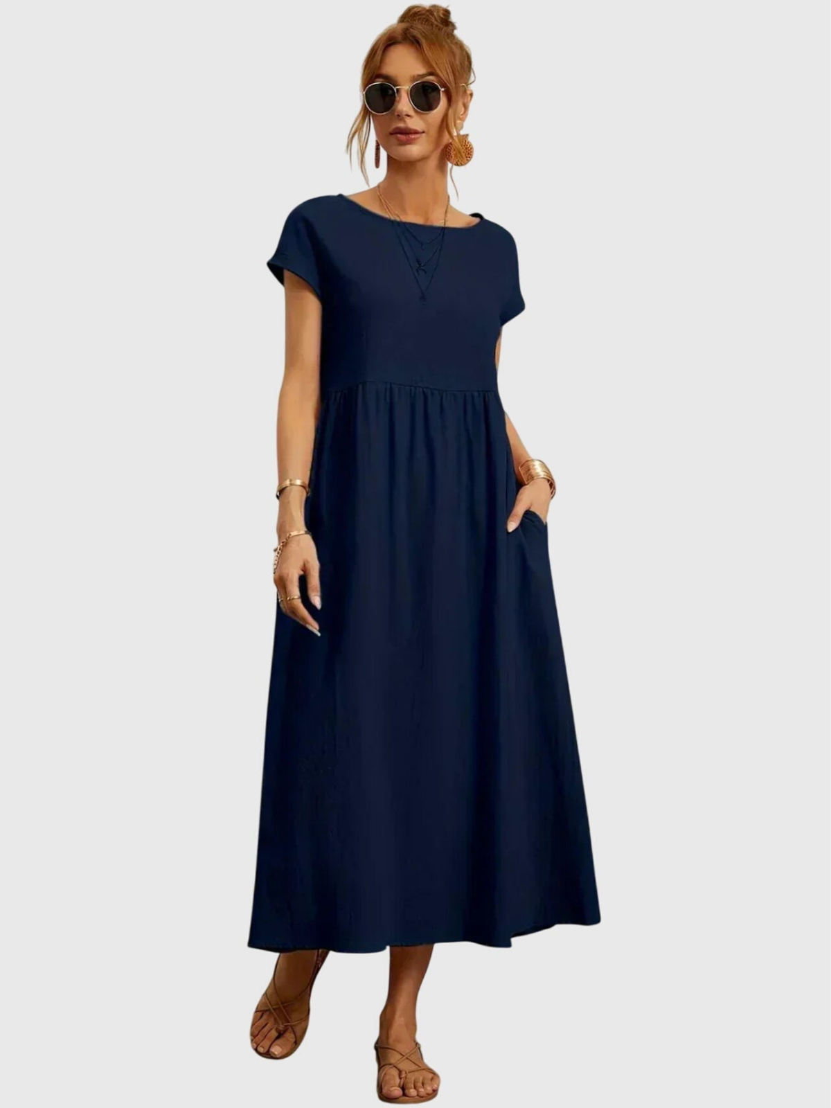 Navy - Woman wearing a solid short sleeve babydoll maxi dress with a gathered waist and hands resting in side pockets.