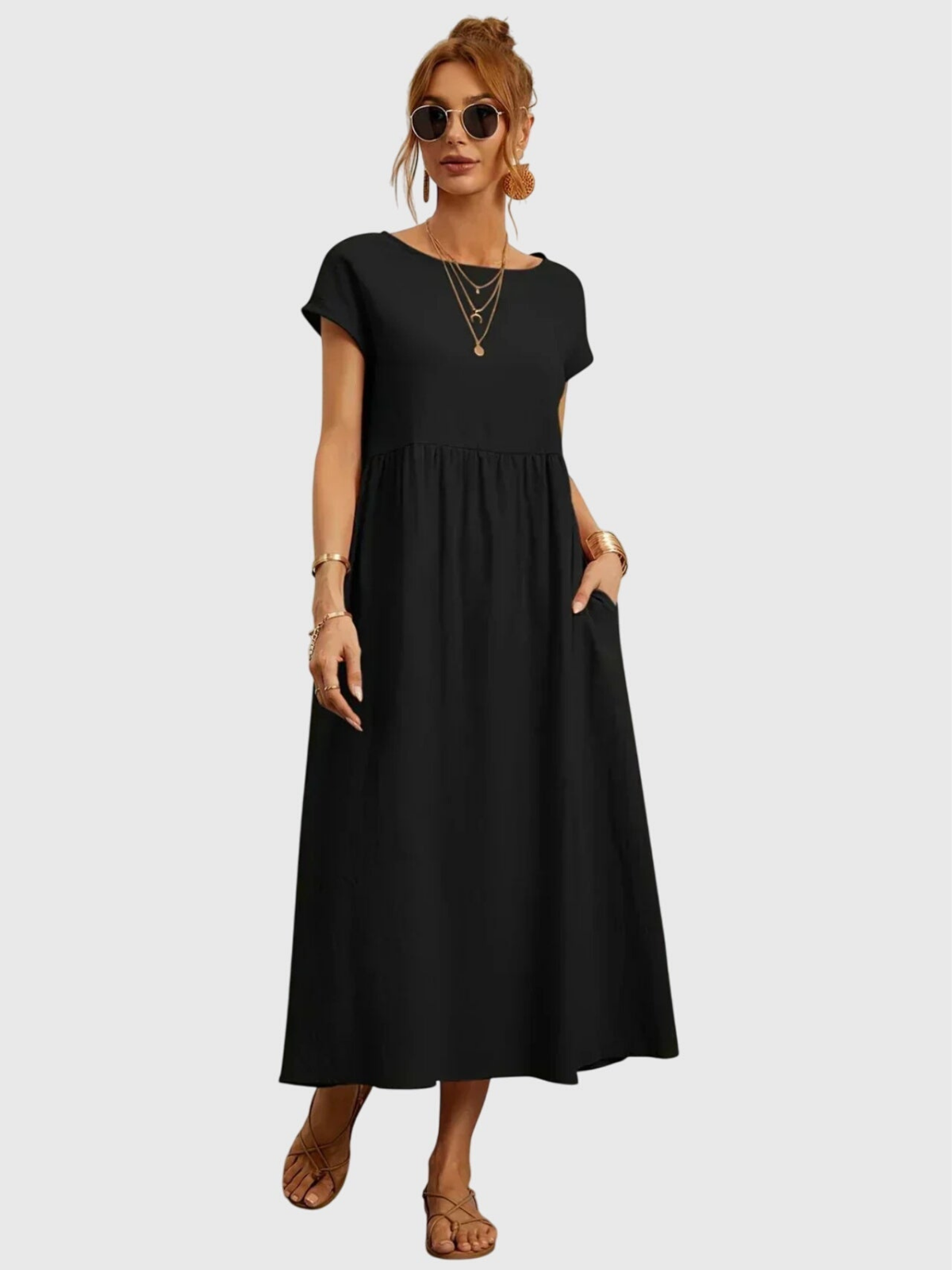 Black - Woman wearing a solid short sleeve babydoll maxi dress with a gathered waist and hands resting in side pockets.