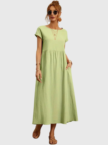 Light Green - Woman wearing a solid short sleeve babydoll maxi dress with a gathered waist and hands resting in side pockets.