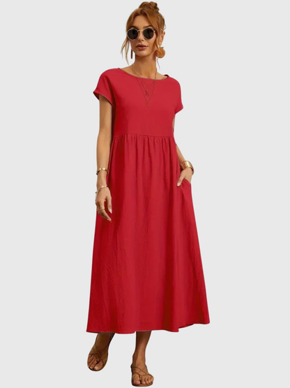 Red - Woman wearing a solid short sleeve babydoll maxi dress with a gathered waist and hands resting in side pockets.