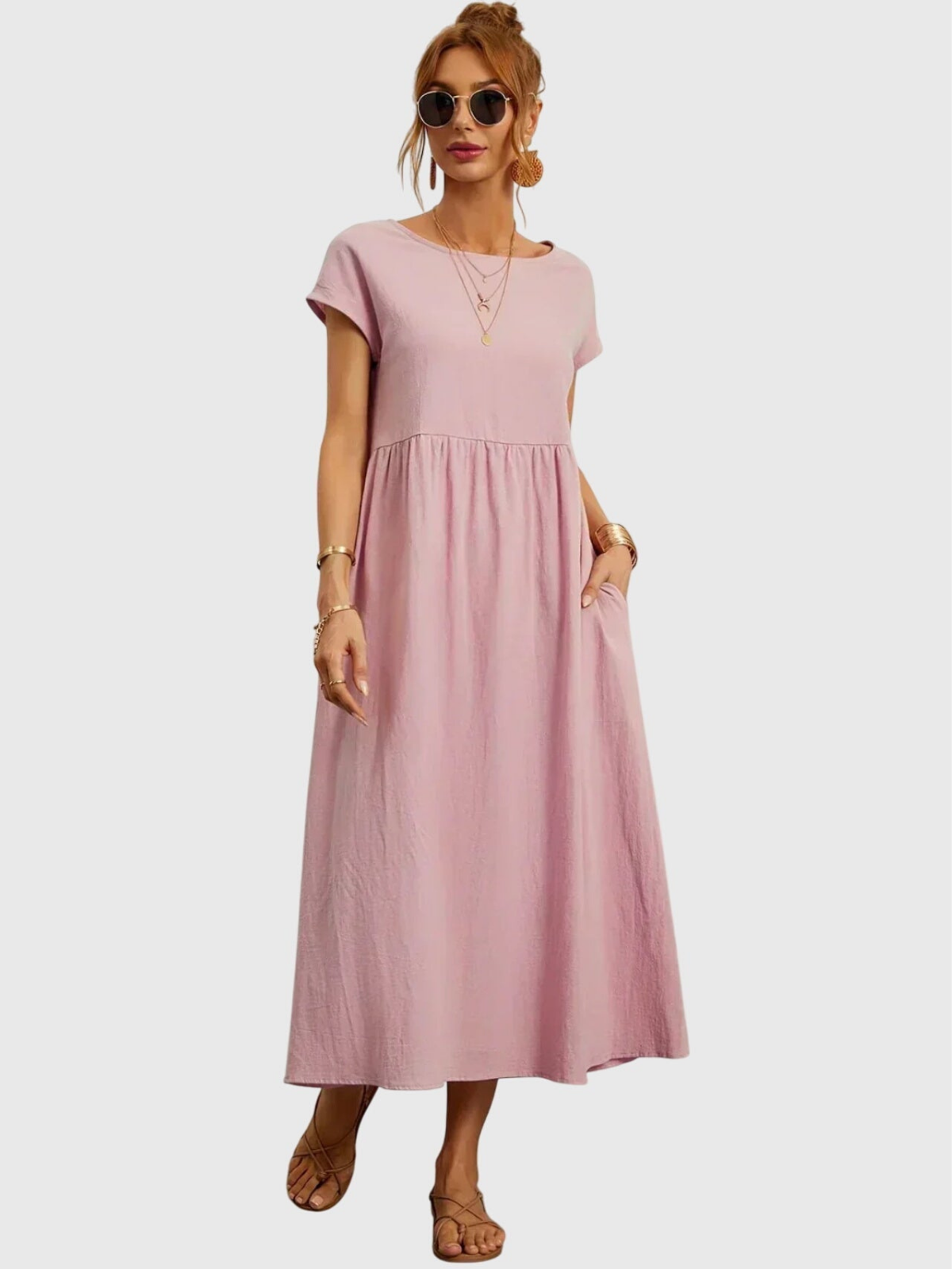 Pink - Woman wearing a solid short sleeve babydoll maxi dress with a gathered waist and hands resting in side pockets.