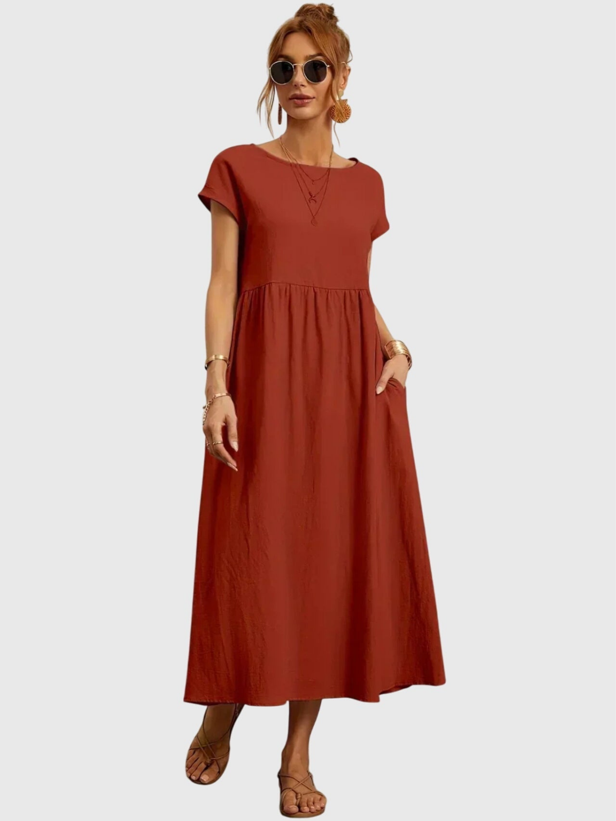 Rust - Woman wearing a solid short sleeve babydoll maxi dress with a gathered waist and hands resting in side pockets.