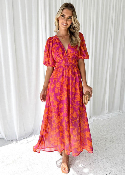 Orange - A woman smiling in a vibrant pink and orange floral print chiffon maxi dress with a deep V-neckline, short puff sleeves, and a smocked waist.