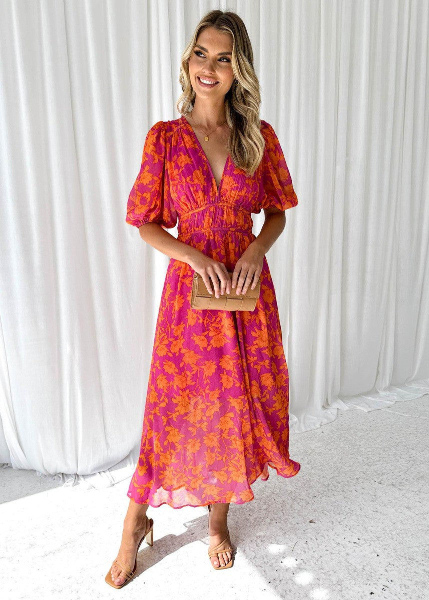 Orange - A woman smiling in a vibrant pink and orange floral print chiffon maxi dress with a deep V-neckline, short puff sleeves, and a smocked waist.