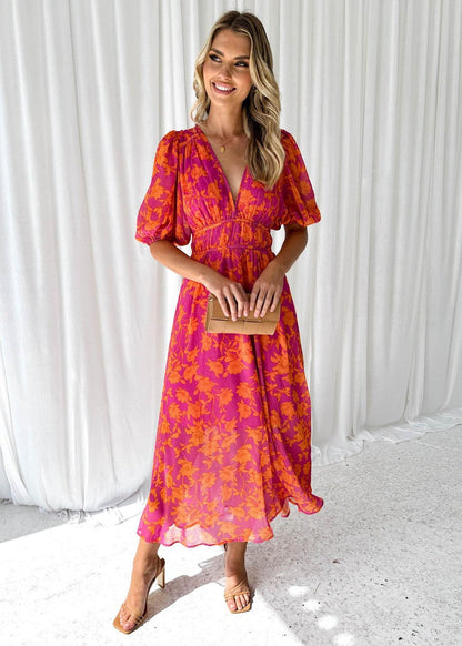 Orange - A woman smiling in a vibrant pink and orange floral print chiffon maxi dress with a deep V-neckline, short puff sleeves, and a smocked waist.