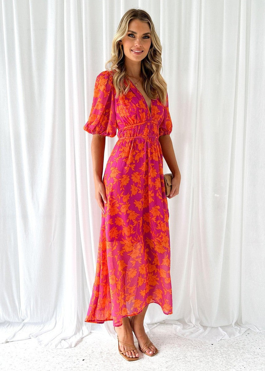 Orange - A woman smiling in a vibrant pink and orange floral print chiffon maxi dress with a deep V-neckline, short puff sleeves, and a smocked waist.