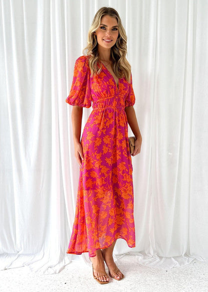 Orange - A woman smiling in a vibrant pink and orange floral print chiffon maxi dress with a deep V-neckline, short puff sleeves, and a smocked waist.