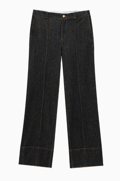 Woman in dark wash denim jumpsuit sitting on a couch