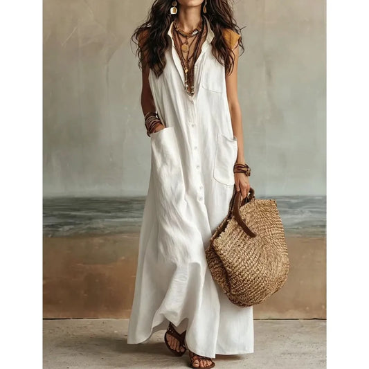 White - Woman wearing a long, sleeveless linen maxi dress with a collar, button-down front, and large patch pockets, holding a woven tote bag.