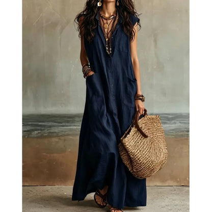 Navy Blue - Woman wearing a long, sleeveless linen maxi dress with a collar, button-down front, and large patch pockets, holding a woven tote bag.