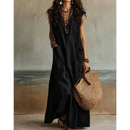 Black - Woman wearing a long, sleeveless linen maxi dress with a collar, button-down front, and large patch pockets, holding a woven tote bag.