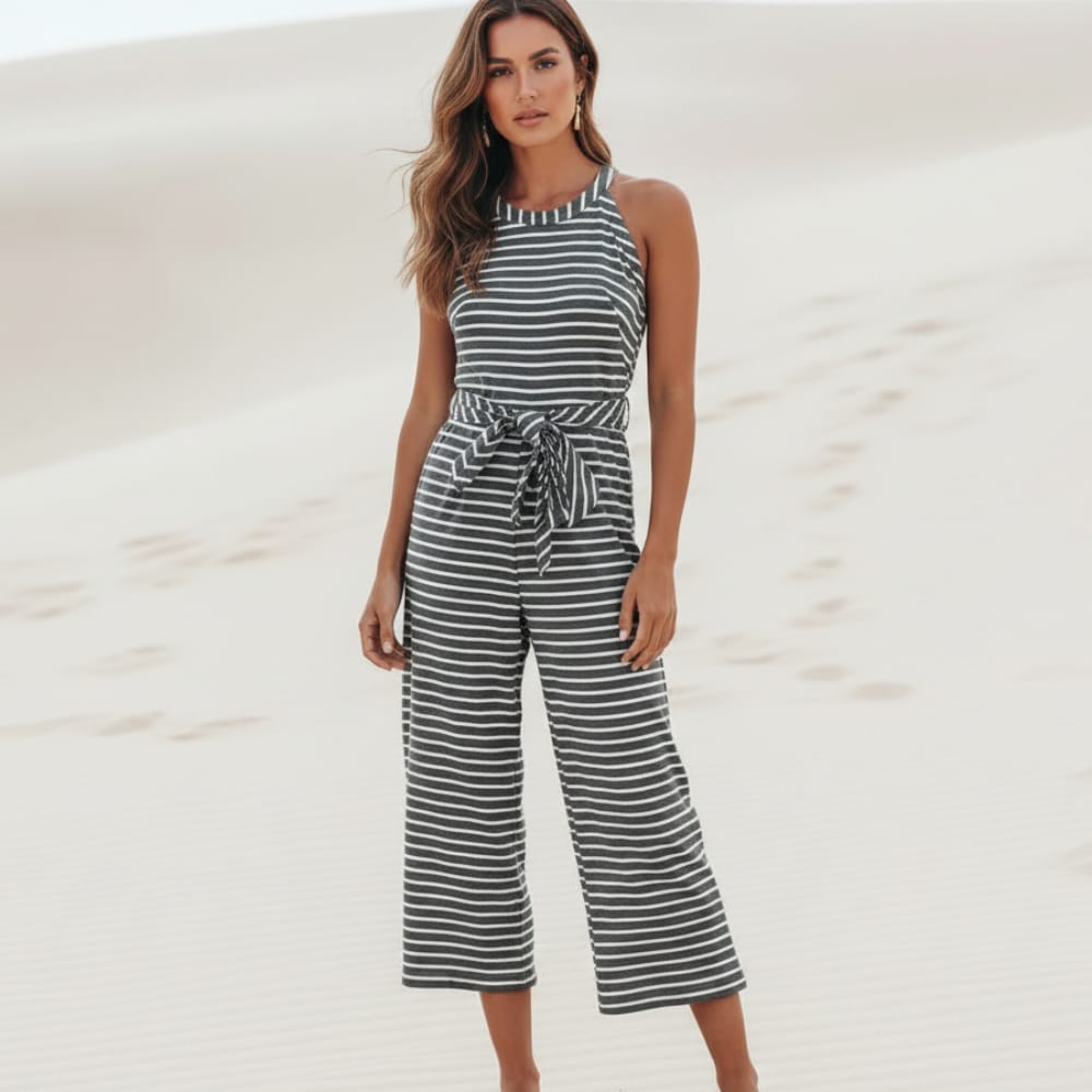 Black - A woman posing in a desert landscape wearing a grey and white horizontally striped knit jumpsuit featuring a high halter neck, a self-tie waist belt, and cropped wide-leg pants.