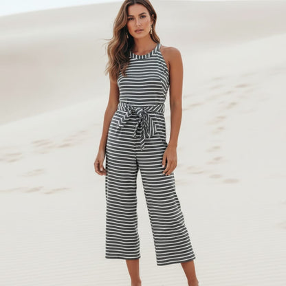 Black - A woman posing in a desert landscape wearing a grey and white horizontally striped knit jumpsuit featuring a high halter neck, a self-tie waist belt, and cropped wide-leg pants.
