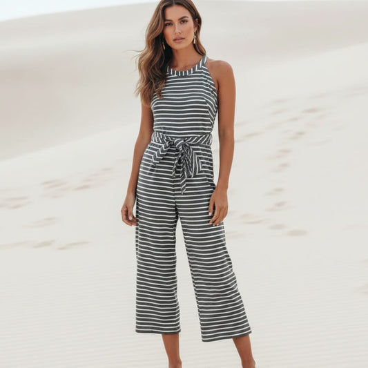 Black - A woman posing in a desert landscape wearing a grey and white horizontally striped knit jumpsuit featuring a high halter neck, a self-tie waist belt, and cropped wide-leg pants.