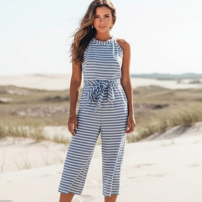 Blue - A woman posing in a desert landscape wearing a grey and white horizontally striped knit jumpsuit featuring a high halter neck, a self-tie waist belt, and cropped wide-leg pants.