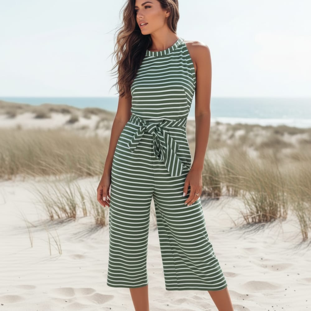 Green - A woman posing in a desert landscape wearing a grey and white horizontally striped knit jumpsuit featuring a high halter neck, a self-tie waist belt, and cropped wide-leg pants.