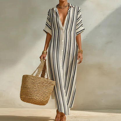 Grey - Woman walking outdoors wearing a long, striped, short-sleeve button-front maxi dress and carrying a woven straw tote bag.