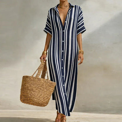 Blue - Woman walking outdoors wearing a long, striped, short-sleeve button-front maxi dress and carrying a woven straw tote bag.