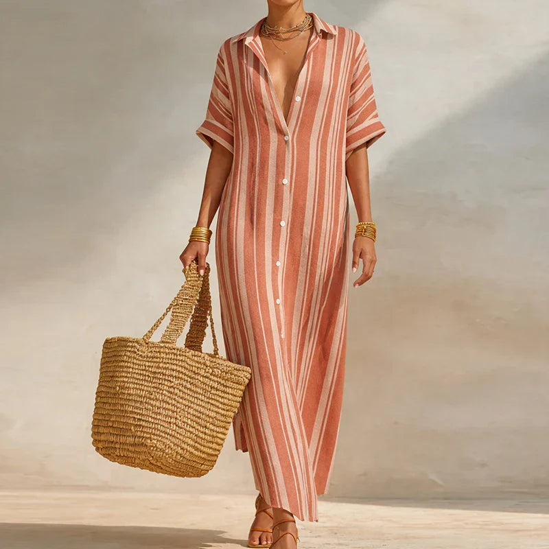 Pink - Woman walking outdoors wearing a long, striped, short-sleeve button-front maxi dress and carrying a woven straw tote bag.