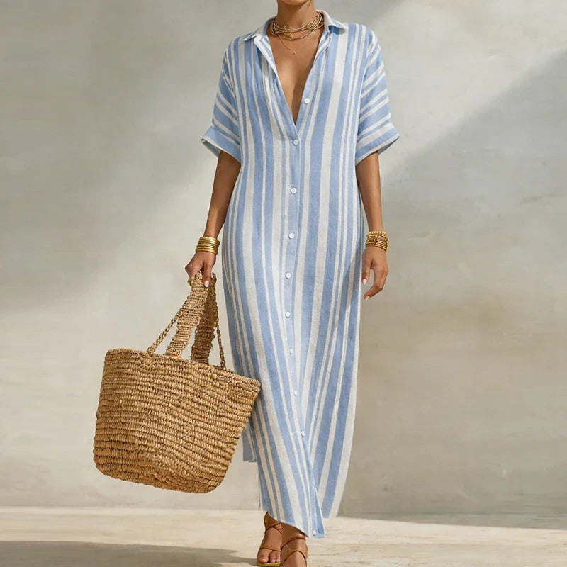 Sky Blue - Woman walking outdoors wearing a long, striped, short-sleeve button-front maxi dress and carrying a woven straw tote bag.