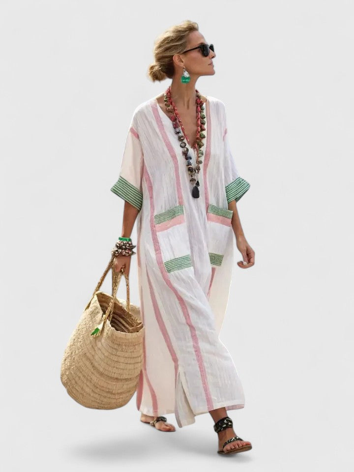 White - Woman walking wearing a long, oversized striped maxi dress with half sleeves, front patch pockets, and side slits, carrying a woven tote bag.