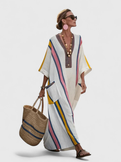 White 2 - Woman walking wearing a long, oversized striped maxi dress with half sleeves, front patch pockets, and side slits, carrying a woven tote bag.