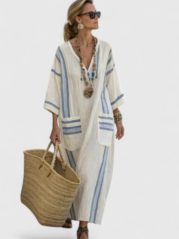 White 3 - Woman walking wearing a long, oversized striped maxi dress with half sleeves, front patch pockets, and side slits, carrying a woven tote bag.