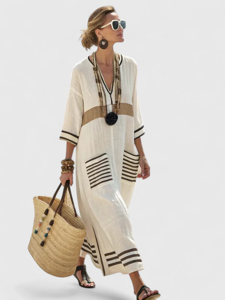 Beige - Woman walking wearing a long, oversized striped maxi dress with half sleeves, front patch pockets, and side slits, carrying a woven tote bag.