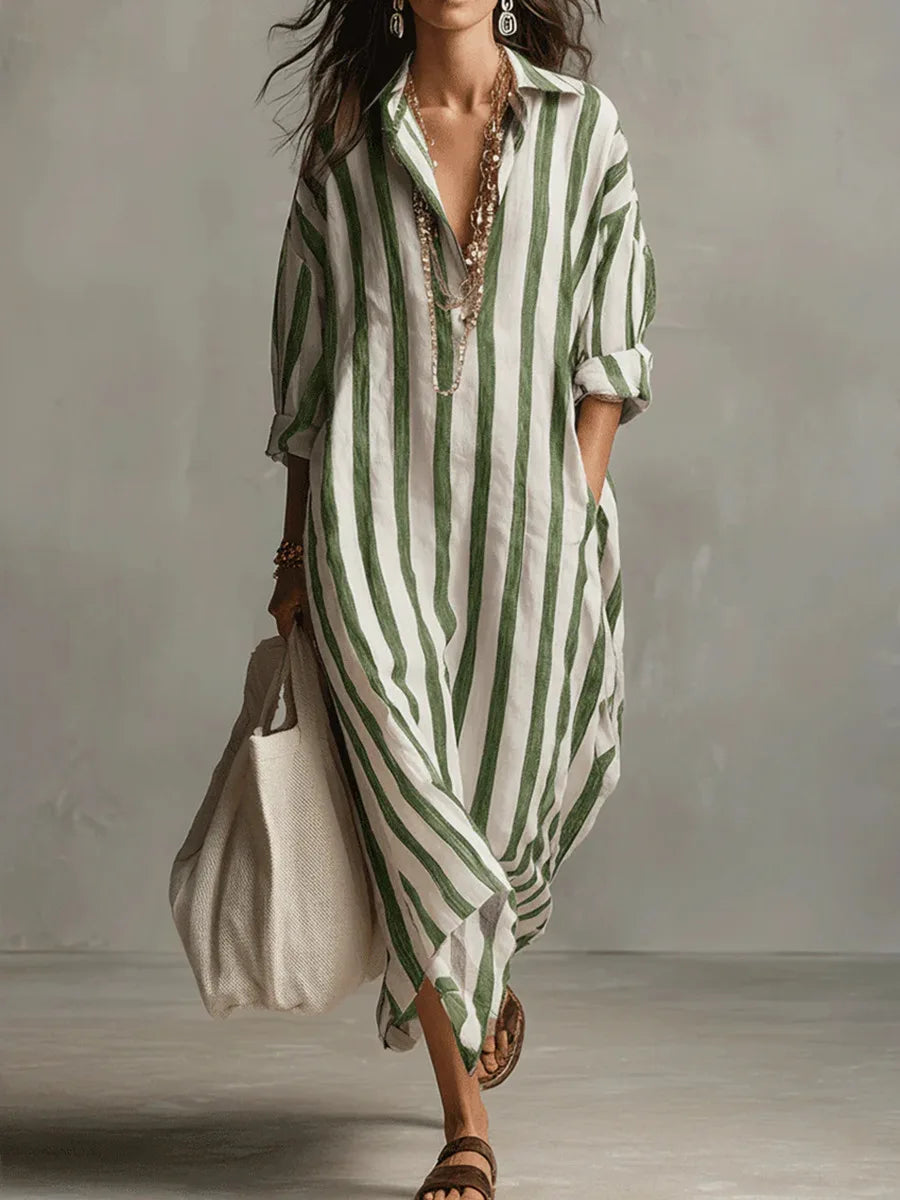 Green - A woman walks wearing an oversized, vertical-striped linen maxi dress in navy and white, featuring a collared V-neck, rolled-up sleeves, and side pockets, paired with a woven tote bag.